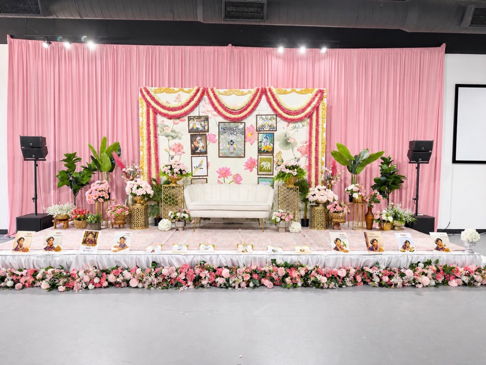 An annaprasana stage with pink draping, lotus panels, framed art and pastel florals