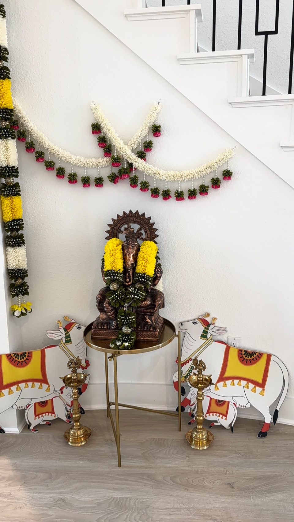 A Ganesha vignette with yellow floral garlands, brass lamps and painted cow cutouts