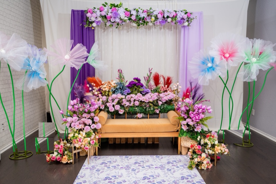 A whimsical garden stage with giant organza flowers, purple drapes and a flower laden daybed