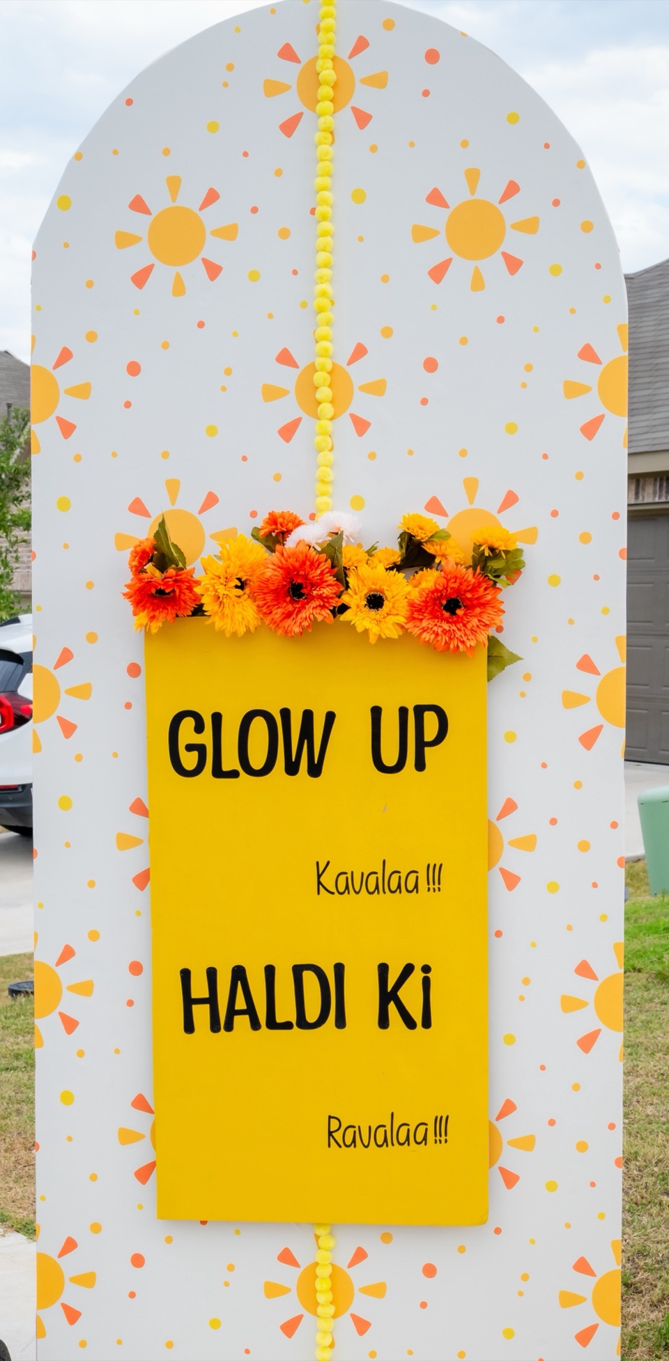 A playful haldi entry board with sun motifs and marigolds reading Glow Up Kavalaa Haldi Ki Ravalaa