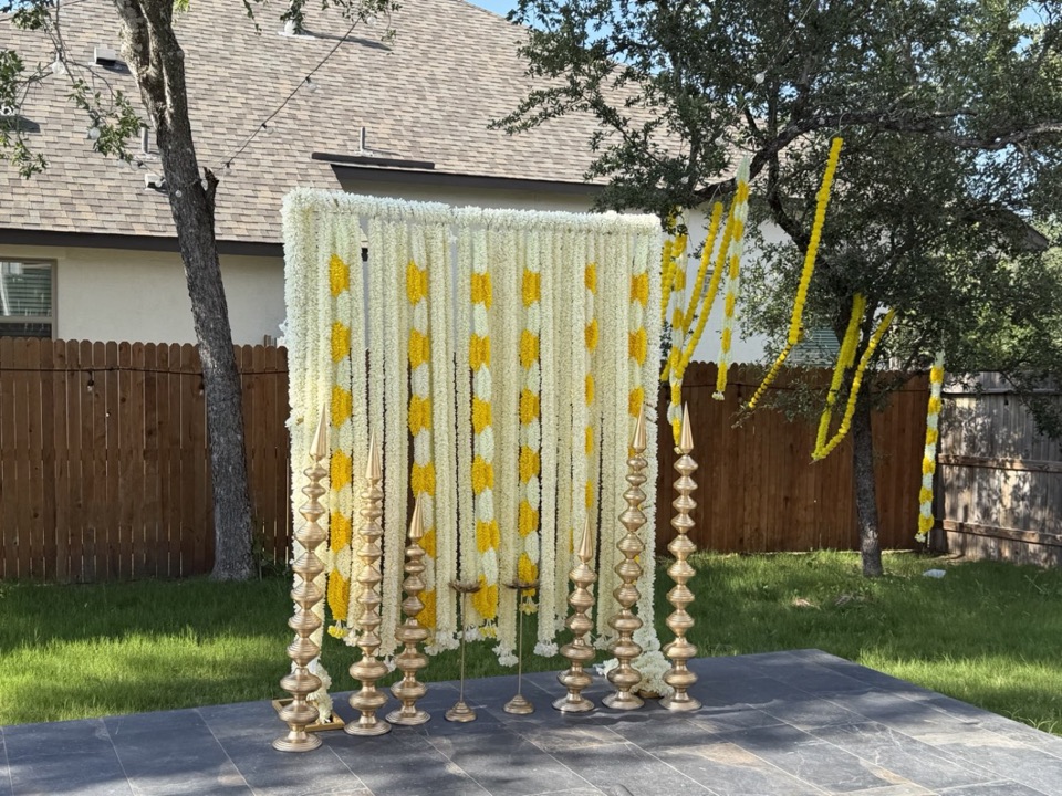 Wall of ivory and yellow garlands with brass lamp stands on a slate patio