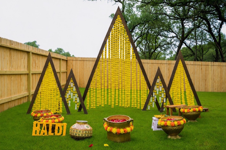 Triangular marigold garland frames on a lawn with brass pots of petals