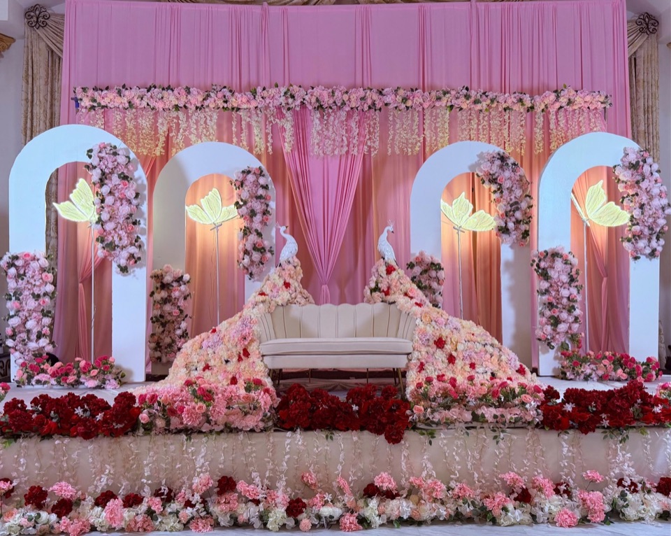 A half saree celebration stage with pink draping, white arches, wisteria strands and rose beds