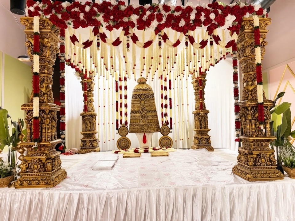 Carved gold mandap with red and ivory garlands framing a grand Balaji backdrop