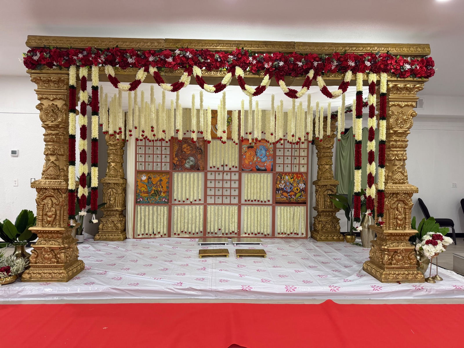 A temple inspired gold mandap with red rose garlands and cascading jasmine strands