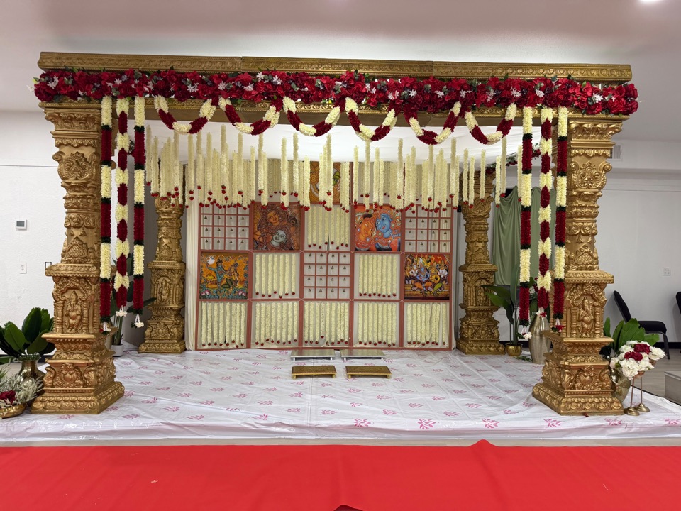 Temple inspired gold mandap with red and ivory garlands in daylight