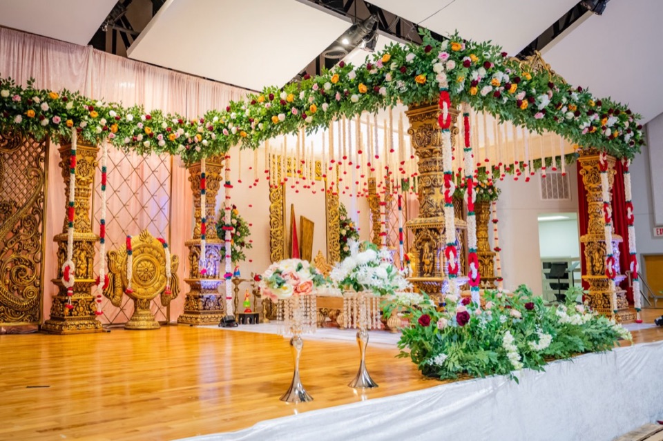 Carved wood mandap with rose garlands seen across a polished ballroom stage