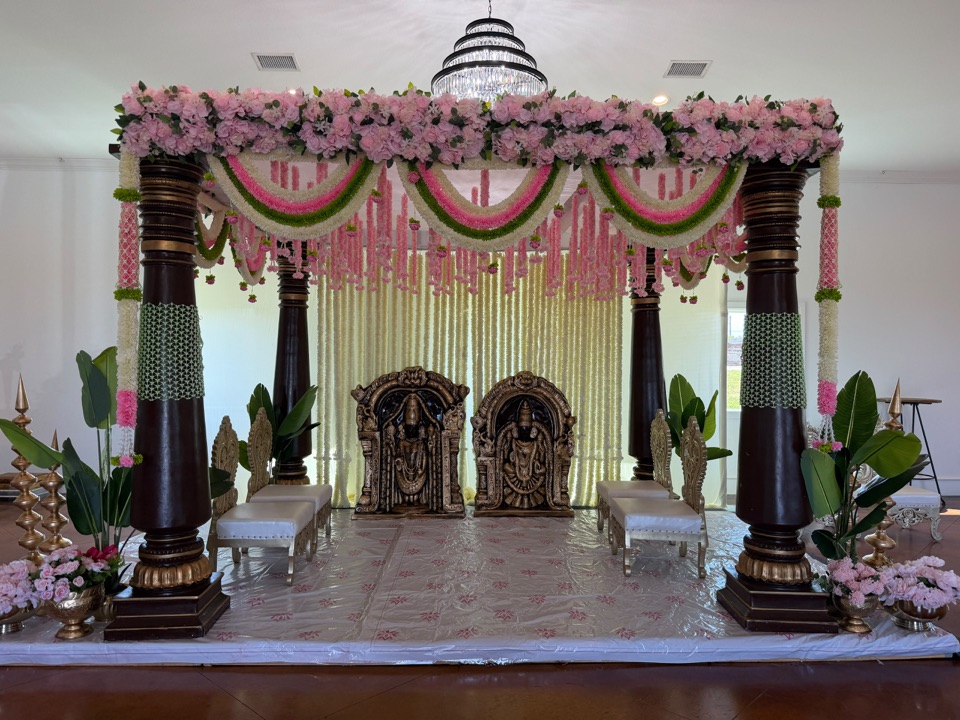 A rosewood pillar mandap layered with blush roses, pink and green garlands and a jasmine curtain