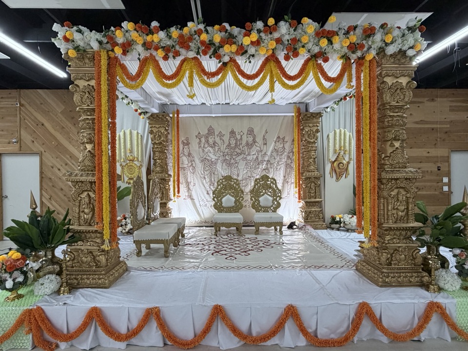 Temple carved mandap with marigold swags, white floral canopy and hand drawn deity backdrop
