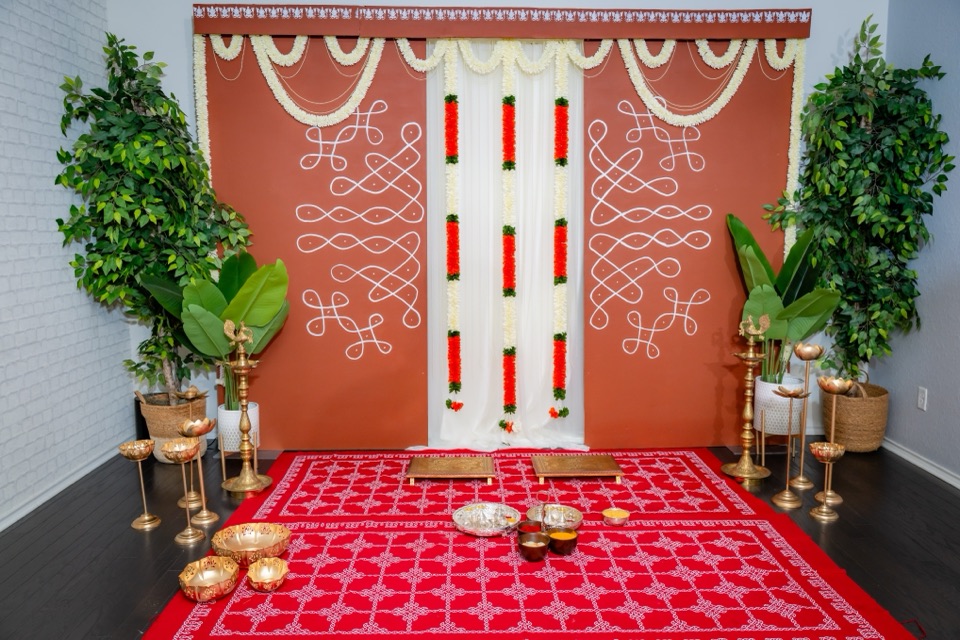 A terracotta backdrop painted with white kolam patterns, jasmine swags and a red kolam print floor