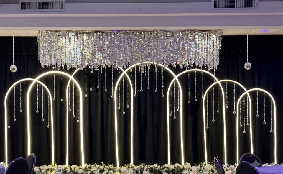 Glowing LED arches with hanging crystal strands and a shimmering sequin canopy over white florals