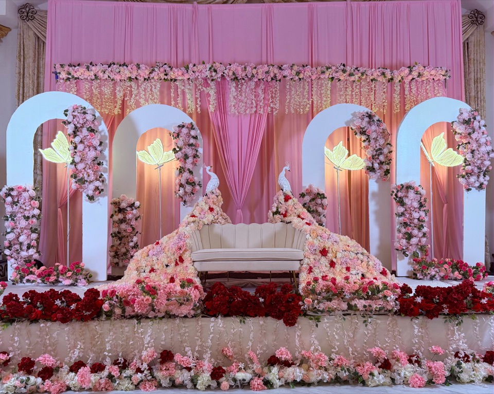 A blush stage with white arches, floral cascades and peacock sculptures
