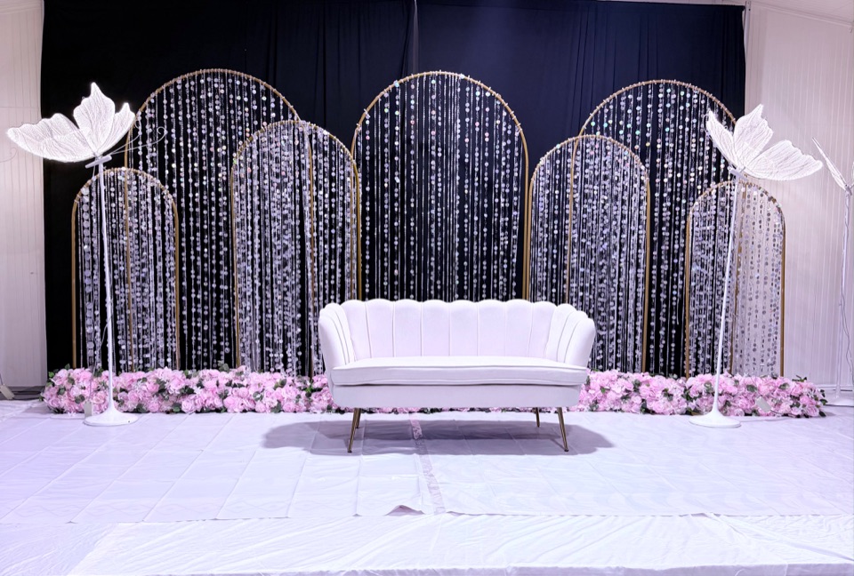 A reception stage with shimmering arches, blush floral borders and a sculptural loveseat