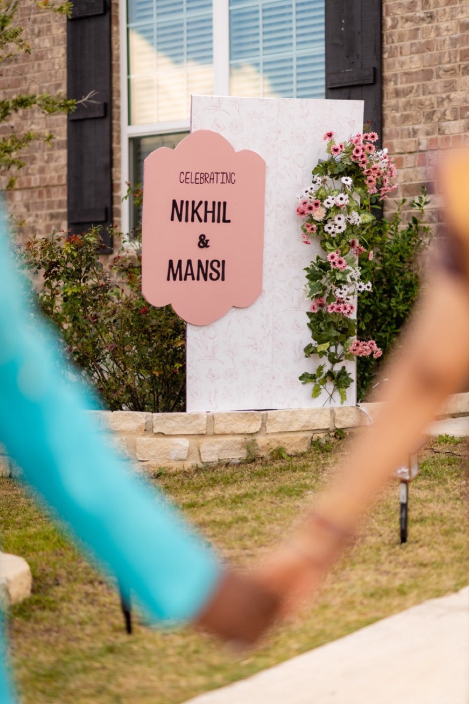 A personalized wedding welcome board with the couple's names, standing among greenery at the venue entrance